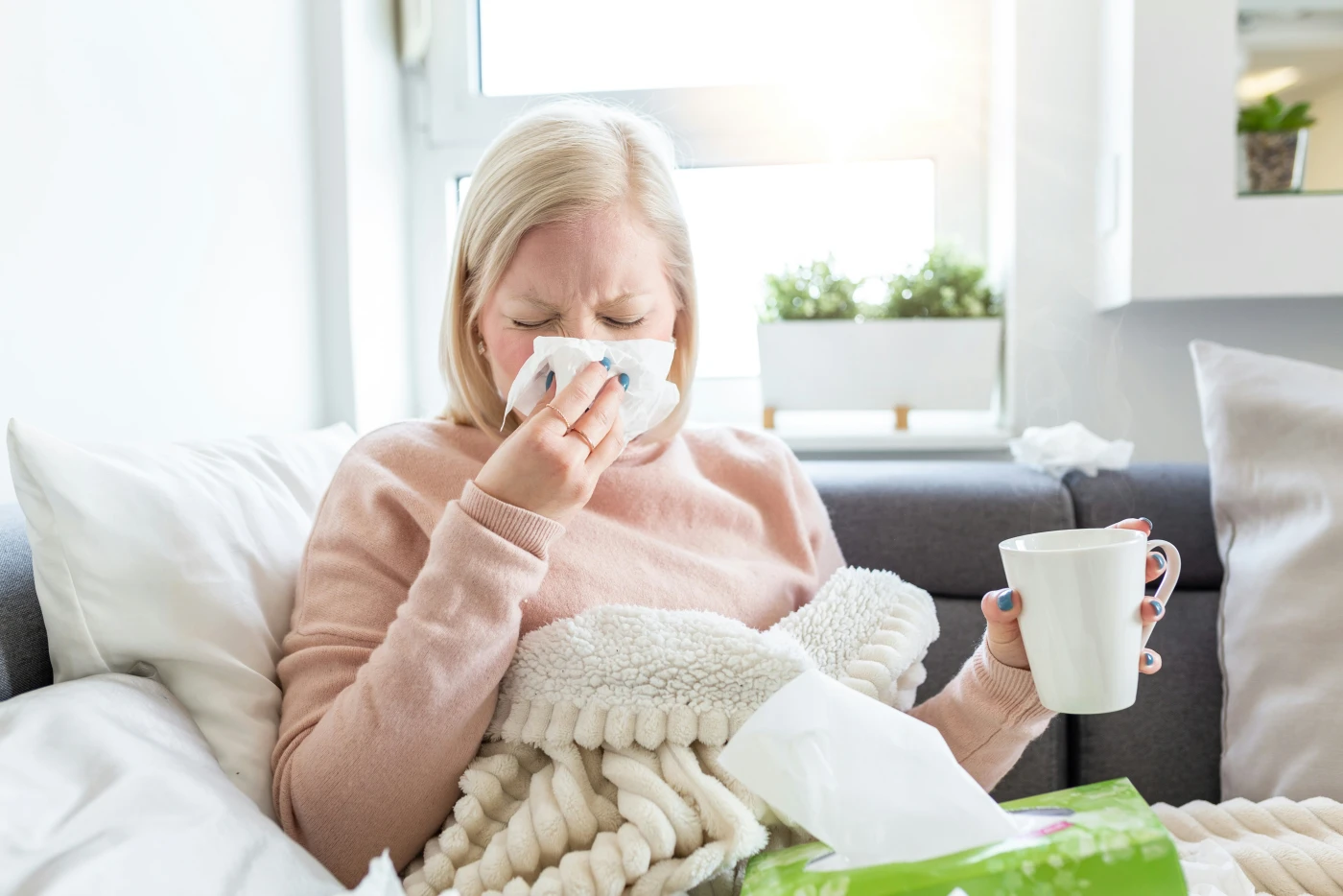 A person resting on a sofa with a tissue and a cup of tea, showing the flu-like phase that resembles early hantavirus symptoms.