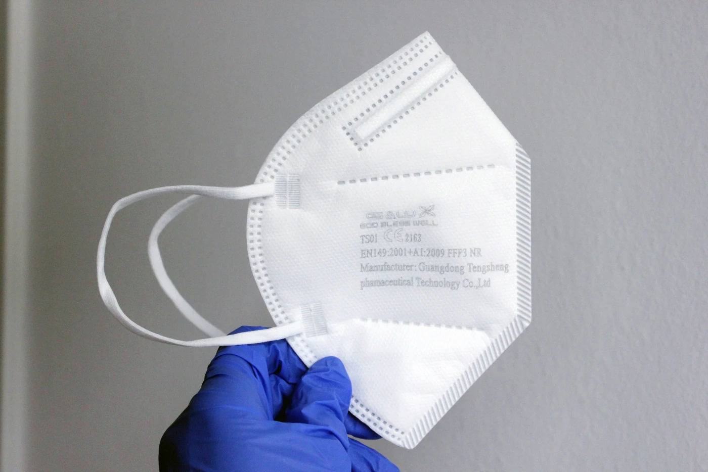 A gloved hand holding a certified FFP3 respirator, the level of mask filtration recommended for cleaning rodent-contaminated spaces.