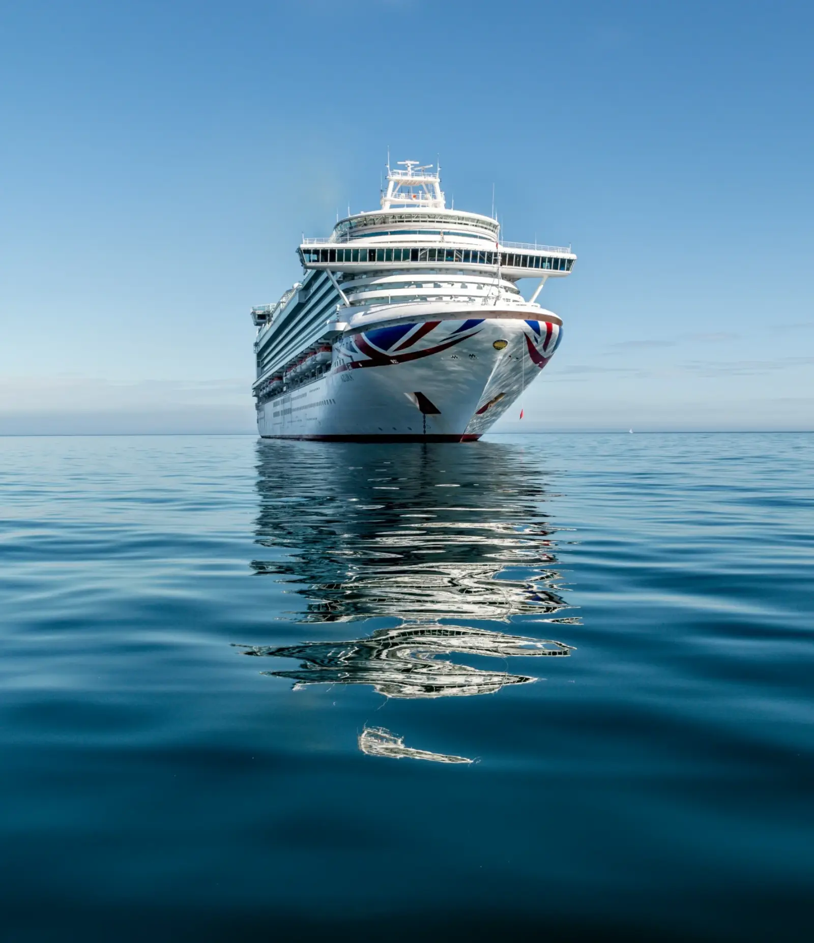 A large white cruise ship anchored on calm open water under a clear sky.